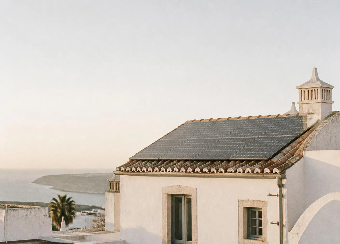 Solar panels on a whitewashed coastal rooftop at sunrise