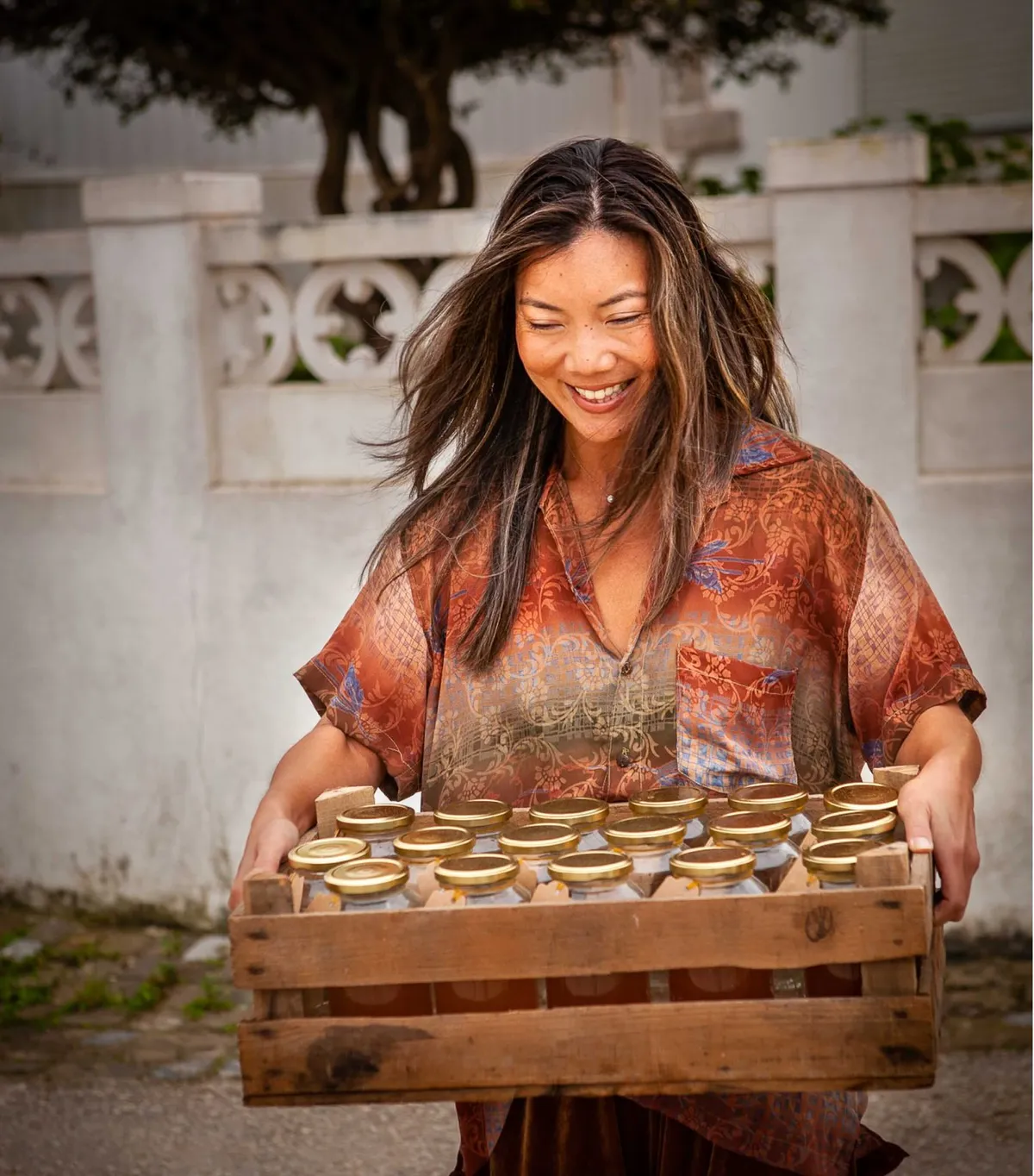 Karen carrying a wooden crate of freshly filled Matsu bone broth jars from her Ericeira kitchen